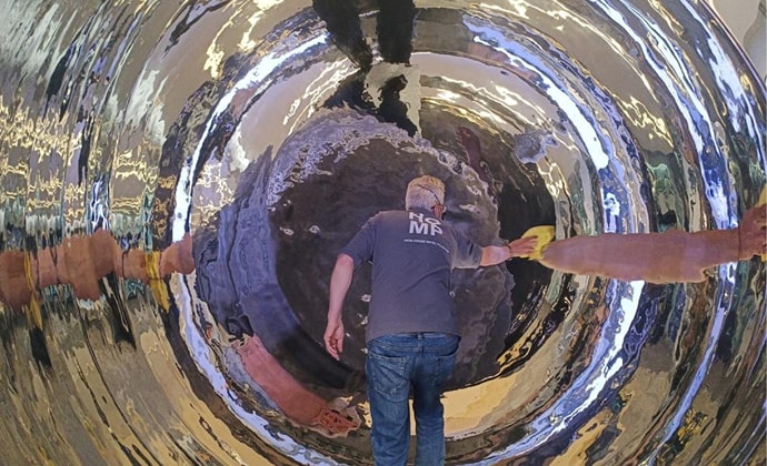 A man meticulously hand polishing Anish Kapoor's stainless steel sculpture 'Turning The World Upside Down III' (1996) at Deutsche Bank, focusing on detailed and careful craftsmanship.